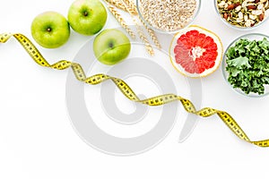 Weight loss concept with oatmeal, nuts, greenery, fruits and measuring tape on white background top view copy space