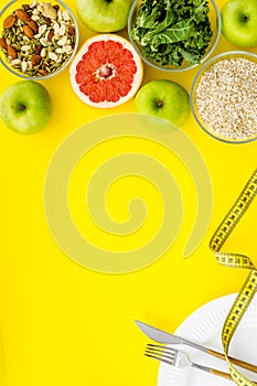 Weight loss concept with oatmeal, nuts, greenery, fruits and measuring tape on yellow background top view copy space