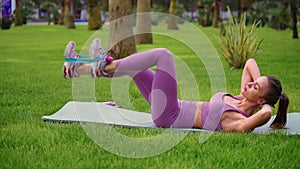 fitness with elastic band, young sporty woman is doing exercise lying on grass in city park