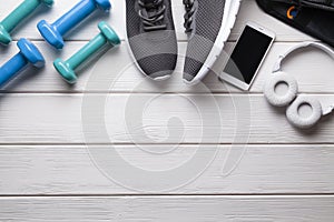 Fitness equipment - colorful dumbbells, sports shoes and smartphone with headphones on a wooden background