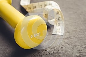 fitness equipment on a dark background/ fitness equipment with yellow dumbbell and measuring tape. Selective focus