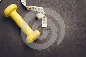 fitness equipment on a dark background/ fitness equipment with yellow dumbbell and measuring tape. Top view and copy space