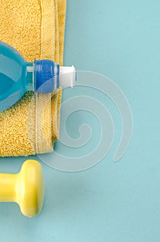 Fitness equipment with dumbbells, towel and bottle/yellow dumbbell, towel and bottle on a blue background. Copy space