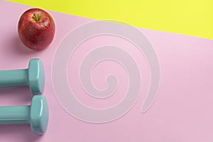 Fitness equipment with healthy food.Apple and two dumbbells on two colors creative background.Healthy lifestyle , sport and home