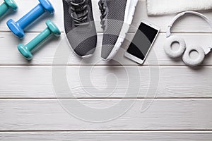 Fitness equipment - sports shoes, dumbbells, towel and smartphone with headphones on a wooden background