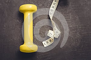 fitness equipment with yellow dumbbel on a dark background/ fitness equipment with yellow dumbbell and measuring tape. Top view