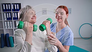 fitness exercise for elderly in room, portait of nurse helping active senior woman pumping shoulder muscle using