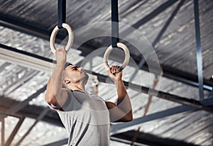 Fitness, exercise man in gymnastics gym during pull up, training or exercise on rings. Young sports athlete or gymnast