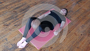 Fitness exercise. A sporty girl lying on a pink rug holds her breath and holds the ball between her knees. The room with the old p