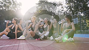 Fitness female young team sitting on the sportground`s floor and drinking water after fitness workout