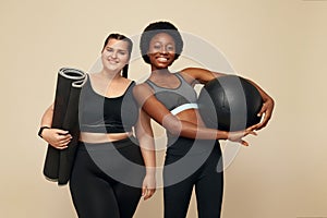 Fitness Friends. Slim And Plus Size Models. African And Caucasion Women In Black Sportswear Holding Fitness Ball And Mat.