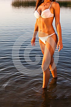 Fitness girl in bikini walking on water. Sunset warm light