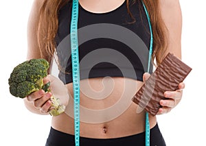 Fitness girl with centimeter tape holds in hand a chocolate bar in another broccoli and on a white isolated background