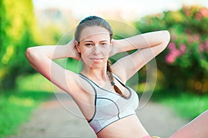 Fitness girl doing crunches in the park before running. Female athlete preparing legs for cardio workout.