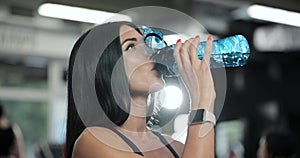 Fitness girl drinking from sport bottle during a workout pause at gym. Portrait of active woman drinking from water