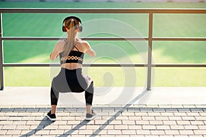 Fitness girl with earphones which doing squat exercises with fabric booty band during her sport workout on special