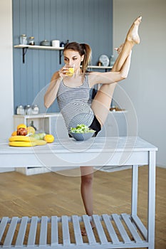 Fitness girl eating healthy food and doing stretching in the kitchen