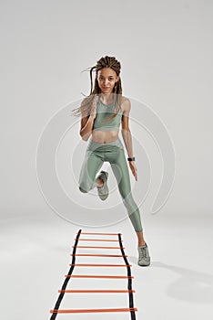 Fitness girl. Full length shot of young sporty mixed race woman in sportswear training on agility ladder drill isolated