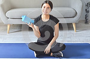 Fitness girl, home and diet concept - smiling teenage girl sitting on mat with sports equipment at home