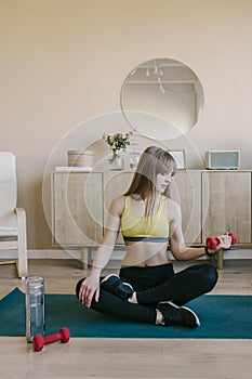 Fitness girl in at home raises the bar up at the floor. She wears yellow sporing t-shirt photo