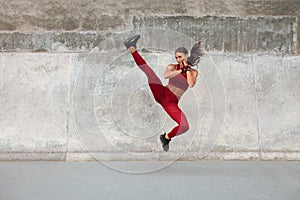 Fitness Girl Kicking. Full-Length Portrait Of Sporty Woman With Strong Muscular Body Against Concrete Wall.