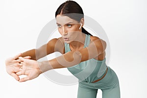 Fitness girl listening music while workout, woman breathing and stretching arms in gym, wearing wireless headphones