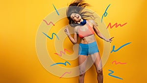 Fitness girl listens to music with headset. Joyful and happy expression on yellow background