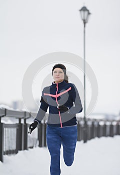 Fitness girl model running at snow winter promenade, jogging