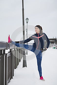 Fitness girl in pink sneakers doing stretching outside at cloudy winter day