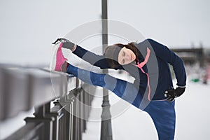 Fitness girl with pink sneakers doing stretching outside at snow winter day