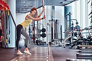 Fitness girl posing for a camera while leaning on a barbell in the modern gym
