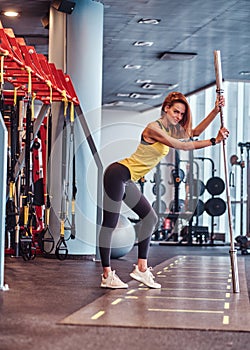 Fitness girl posing for a camera while leaning on a barbell in the modern gym