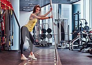 Fitness girl posing for a camera while leaning on a barbell in the modern gym