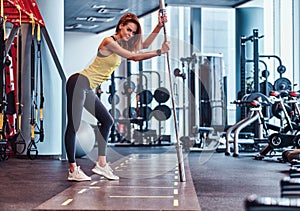 Fitness girl posing for a camera while leaning on a barbell in the modern gym