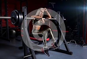 Fitness girl posing in the gym on the bench with barbell