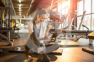 Fitness girl reading good news or message on phone and holding fist up while sitting on mat at gym during exercise