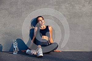 Fitness girl sitting relaxed after workout holding water bottle in her hands, Woman taking a break after exercise