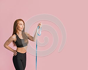 Fitness girl smiling and posing hold measure tape in black sportswear on a pink background. Slim woman with a beautiful athletic