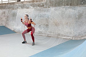 Fitness Girl Squats With Resistance Band. Fit Woman Doing Cardio Workout Outdoors. Sexy Female In Fashion Sporty Outfit.