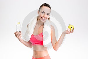 Fitness girl with towel holding bottle of water and apple