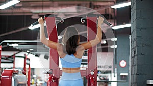 Fitness girl training pull ups exercises in sport machine in gym club. Woman bodybuilder pulling up in fitness machine