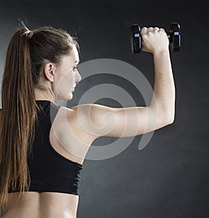 Fitness girl training shoulder muscles lifting dumbbells back view