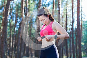 Fitness girl using heart rate monitor for workout in the forest or tracking her weight loss improvement