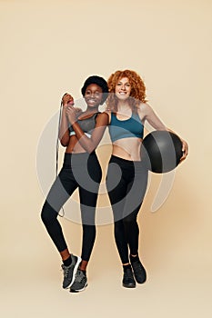 Fitness Girls. African And Caucasian Women Portrait. Smiling Female Holding Exercise Equipment And Looking At Camera.
