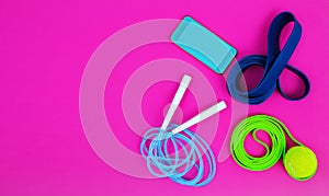 Fitness gum - elastic rubber bands of resistance and a skipping rope on a bright pink background, layout with copy space.