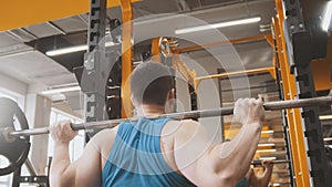 Fitness gym - muscular man performs squats with barbell - rear view