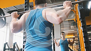 Fitness gym - muscular man performs squats with barbell - rear view