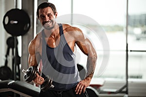 Fitness in gym, sport and healthy lifestyle concept. Handsome athletic man in blue shirt making exercises. Bodybuilder