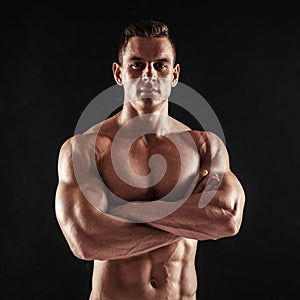 Fitness in gym, sport and healthy lifestyle concept. Handsome athletic man showing his trained body on dark background