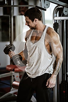 Fitness in gym, sport and healthy lifestyle concept. Handsome athletic man in white shirt making exercises. Bodybuilder